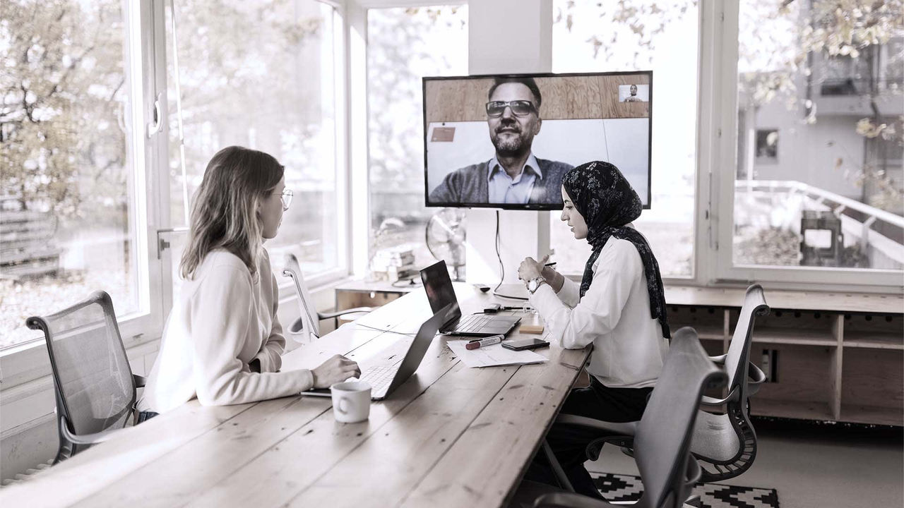 A group of people sitting at a table and watching a video conference.