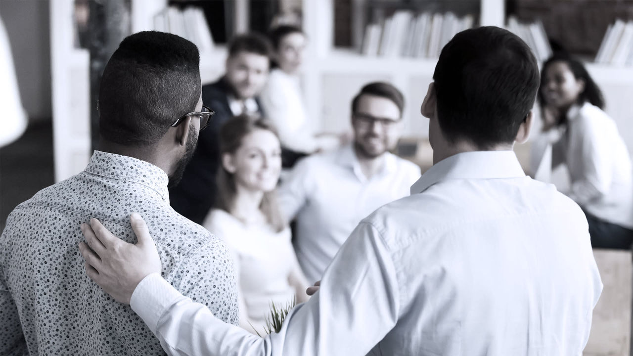 A group of people in a meeting are hugging each other.