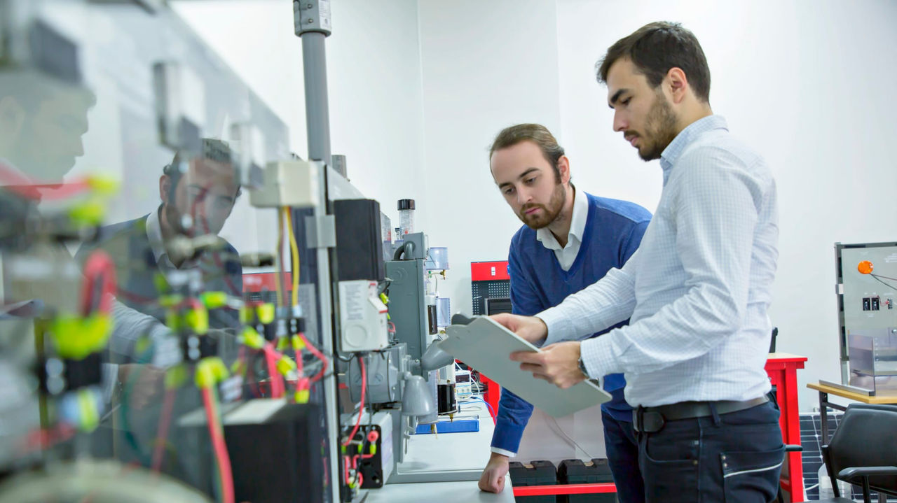 Two men standing in front of a machine in a factory.