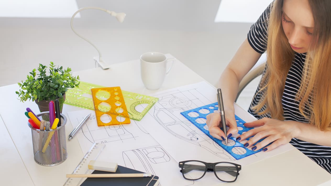Graphic designer apprentice with glasses on a desk, a cup full of pencils and a little plant