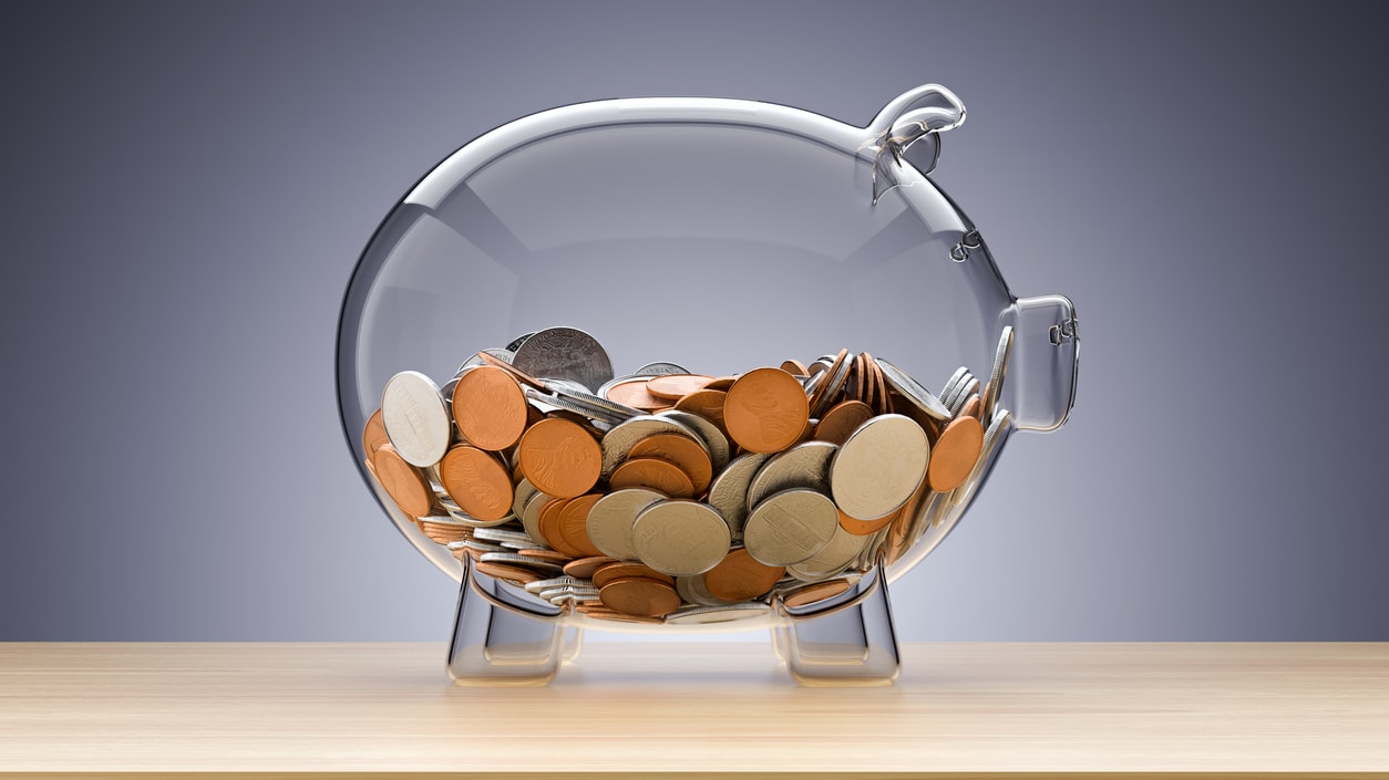 A glass piggy bank filled with coins on a table.