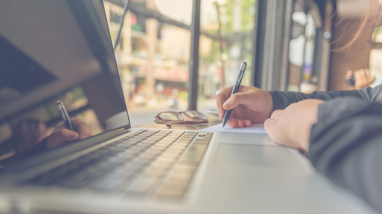 A person writing on a laptop with a pen.