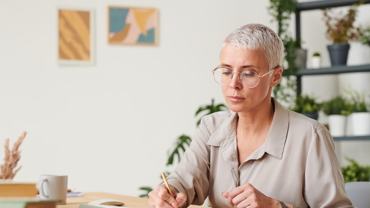 A woman is sitting at a desk and writing in a notebook.