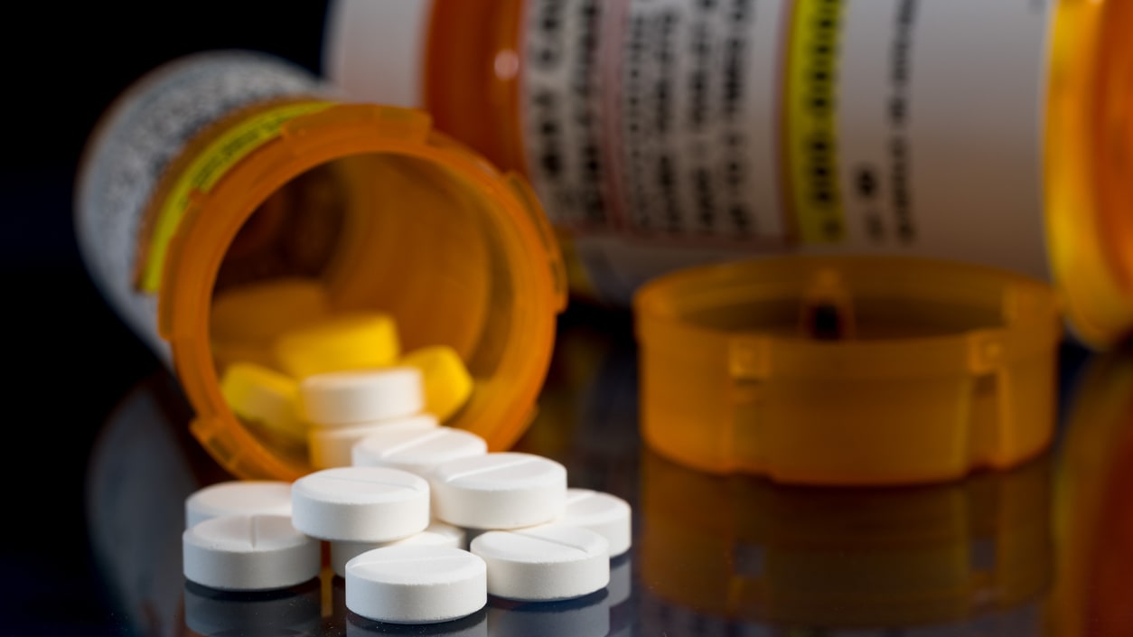 A pill bottle with pills spilling out on a black surface.