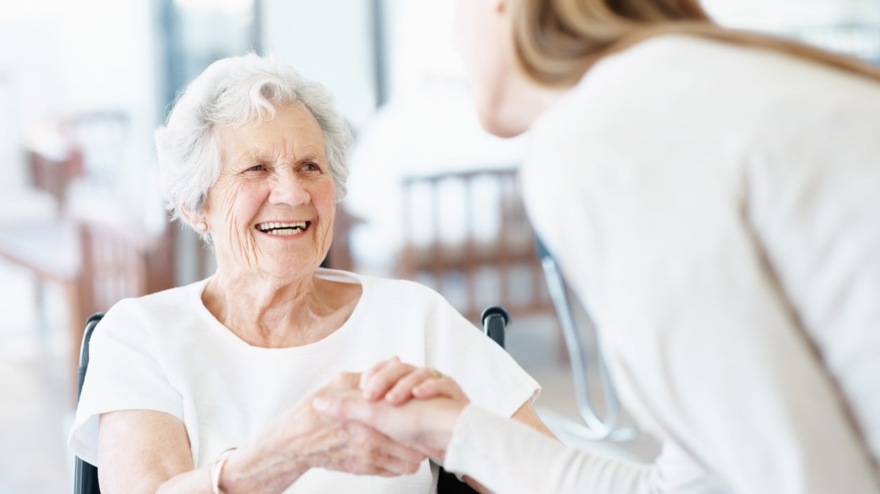 A woman is shaking hands with an elderly woman in a wheelchair.