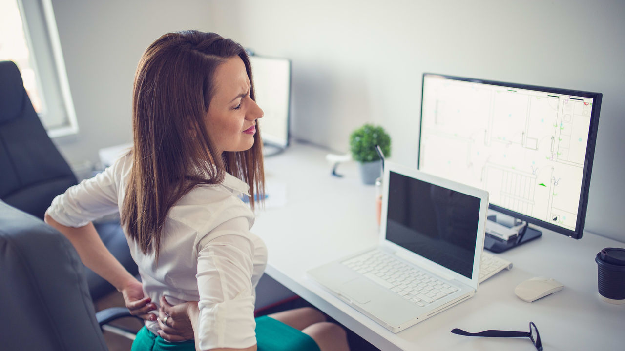 A woman sitting at a desk with her back pain.