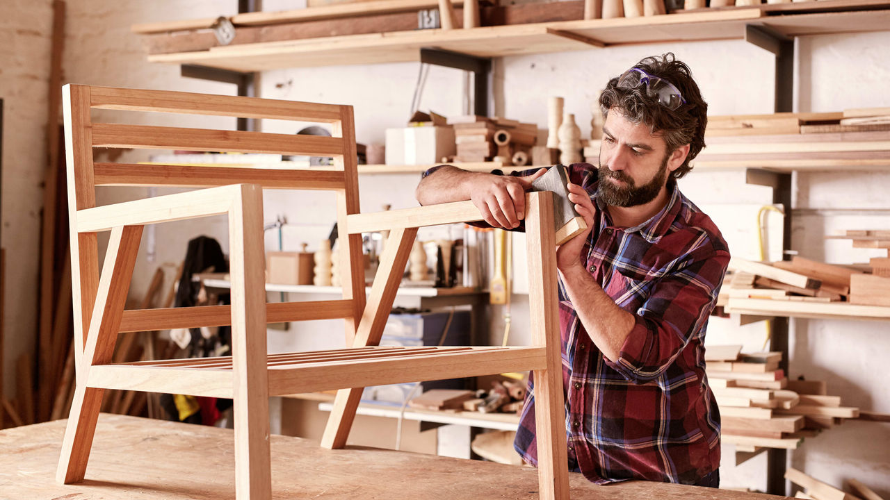 A man is working on a wooden chair in his workshop.