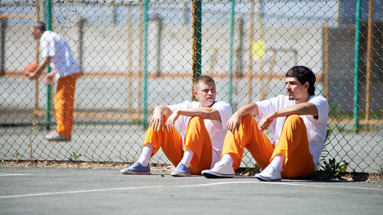 Two men sitting on a court in orange prison uniforms.