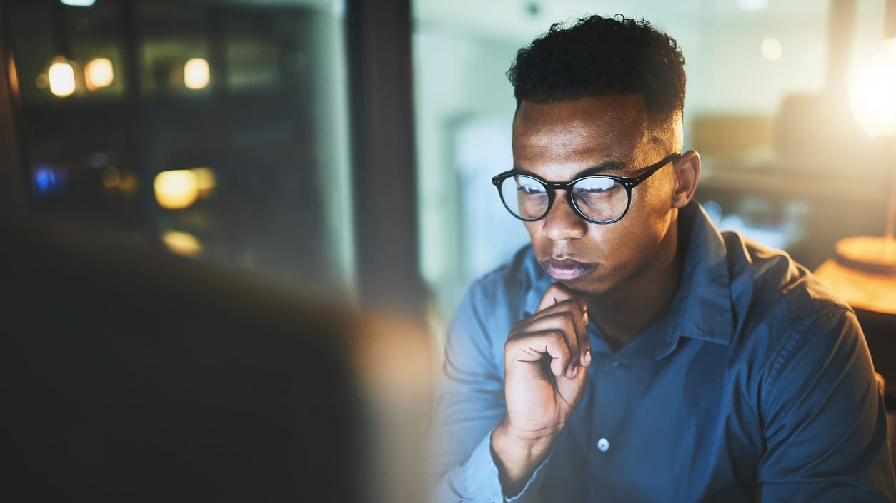 A man in glasses is looking at a computer screen.