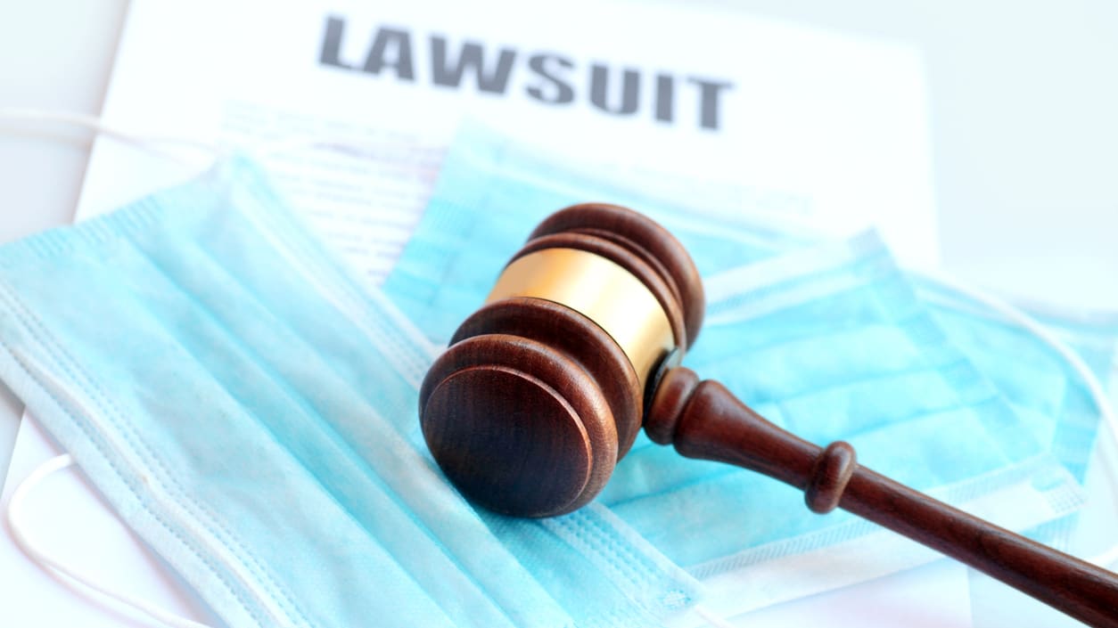 A gavel sits on top of a medical mask and a legal document.