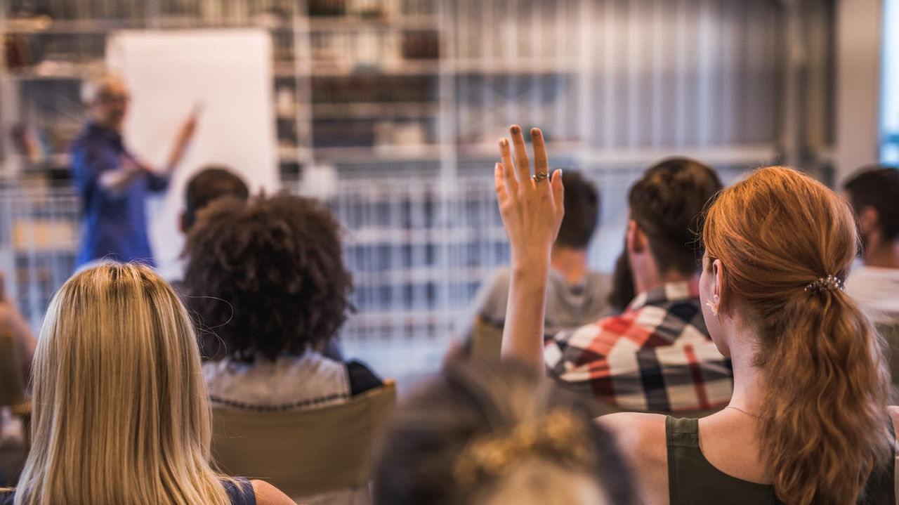 A group of people sitting in a room and raising their hands.