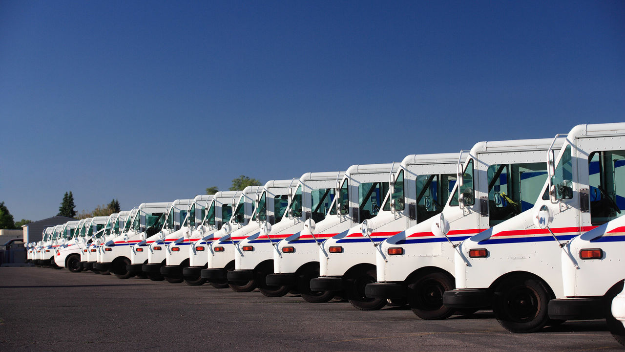 A row of white postal trucks parked in a parking lot.