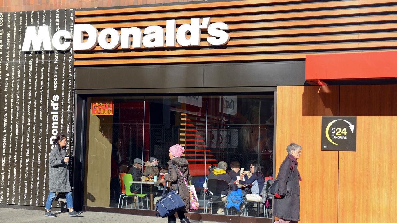 A mcdonald's restaurant with people walking in front of it.