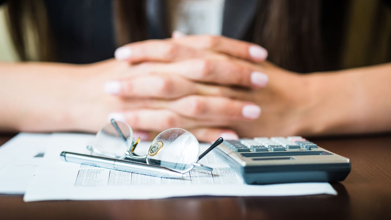 A woman with glasses and a calculator sitting at a desk.