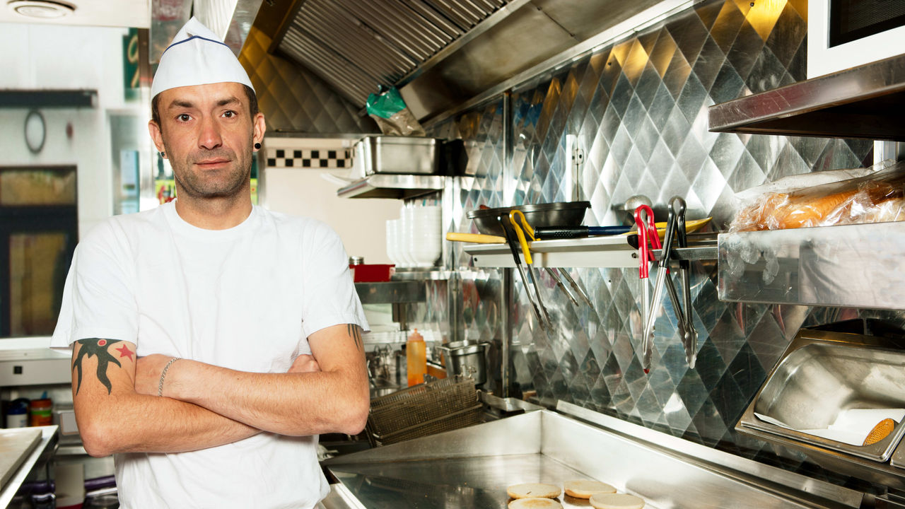 A chef standing in a kitchen with his arms crossed.