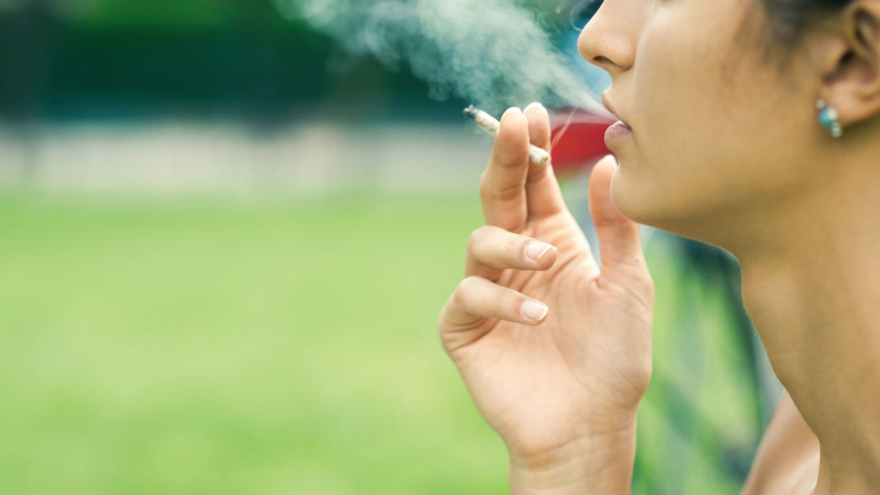 A woman is smoking a cigarette in a park.