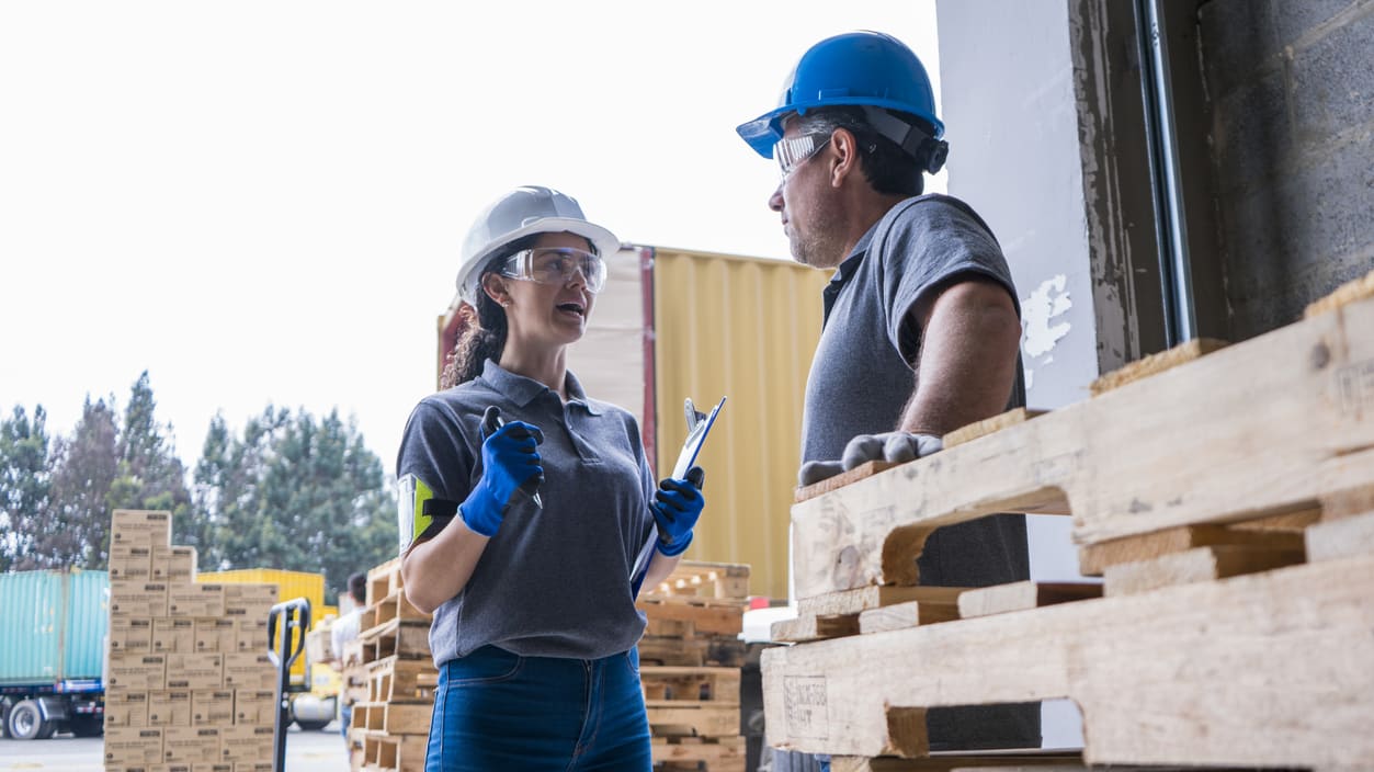 Two workers standing next to pallets in a warehouse.