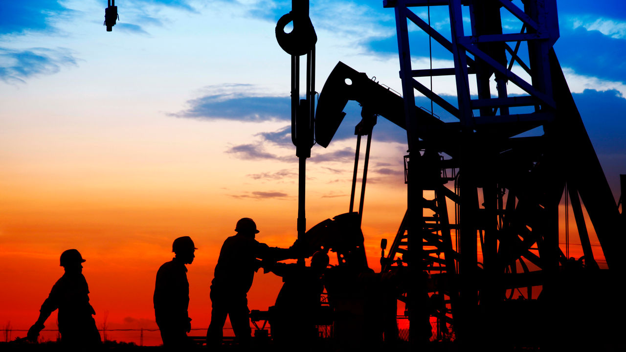 A group of people working on an oil pump at sunset.