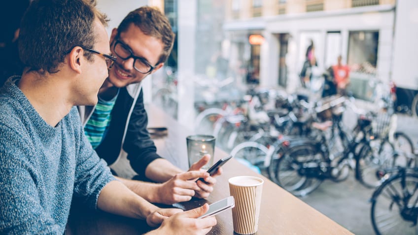 Two men sitting at a table looking at their phones.