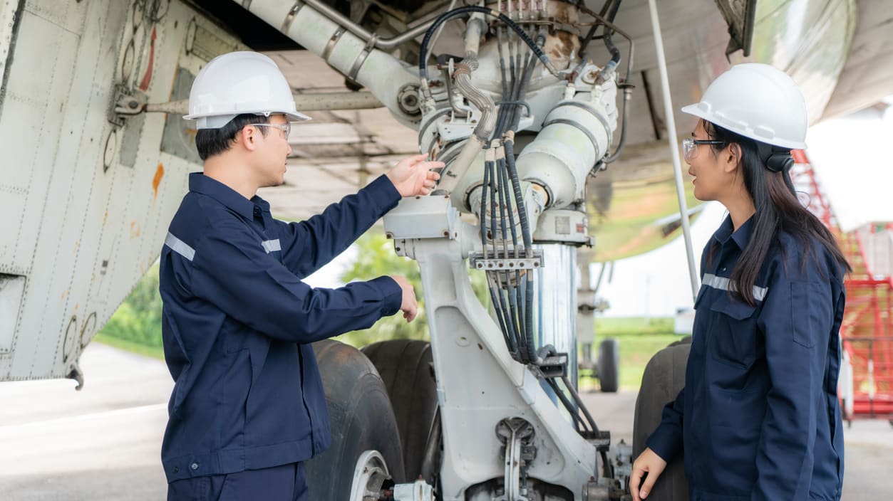 Two asian men working on the engine of an airplane.