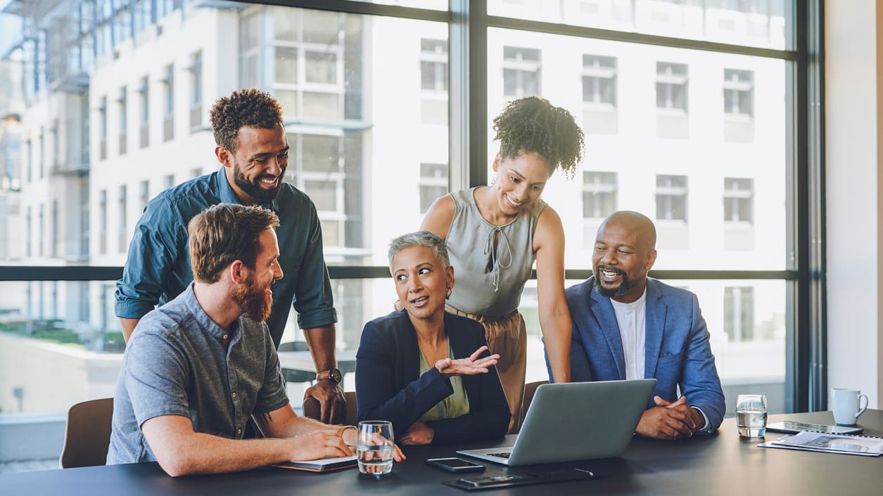 A group of business people sitting around a table and looking at a laptop.