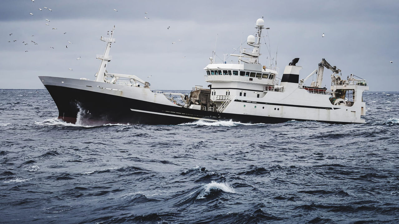 A boat in the ocean with birds flying around it.