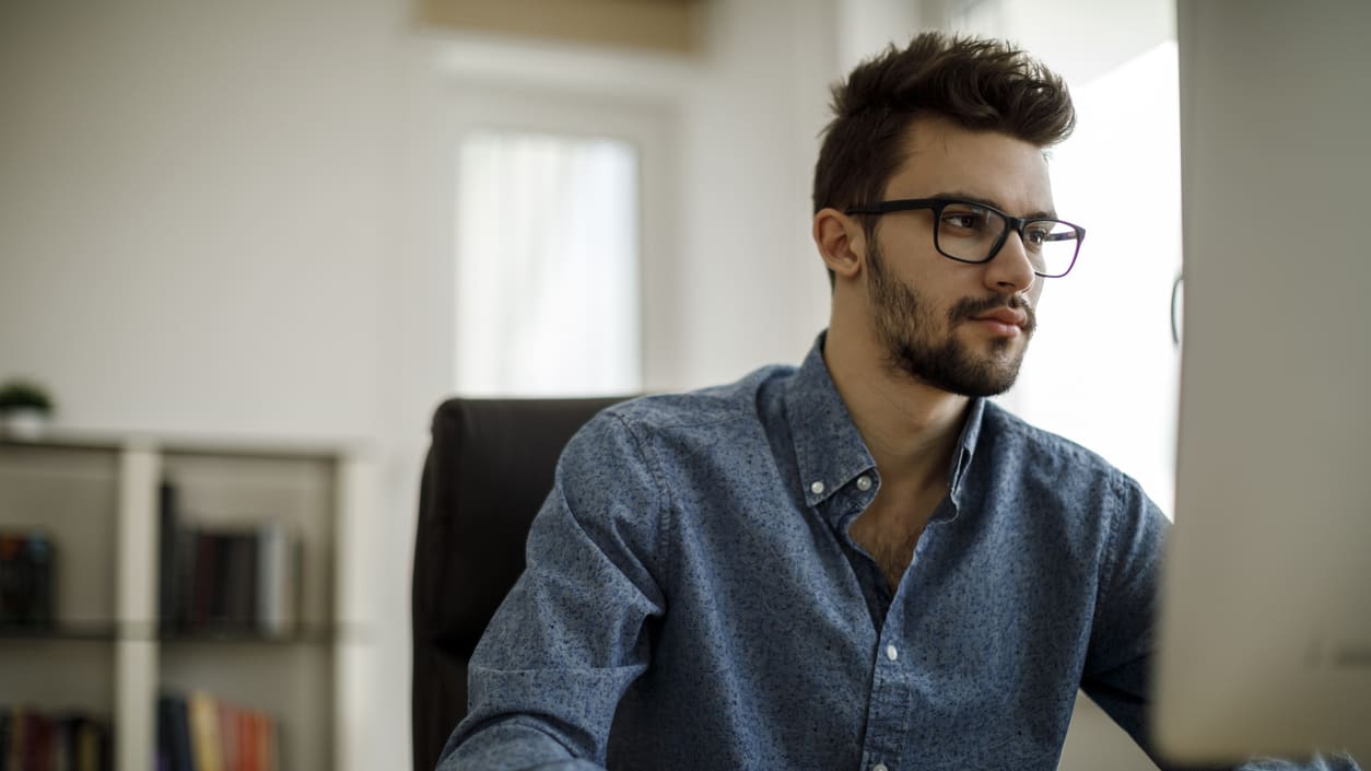 A man wearing glasses is sitting at a desk in front of a computer.