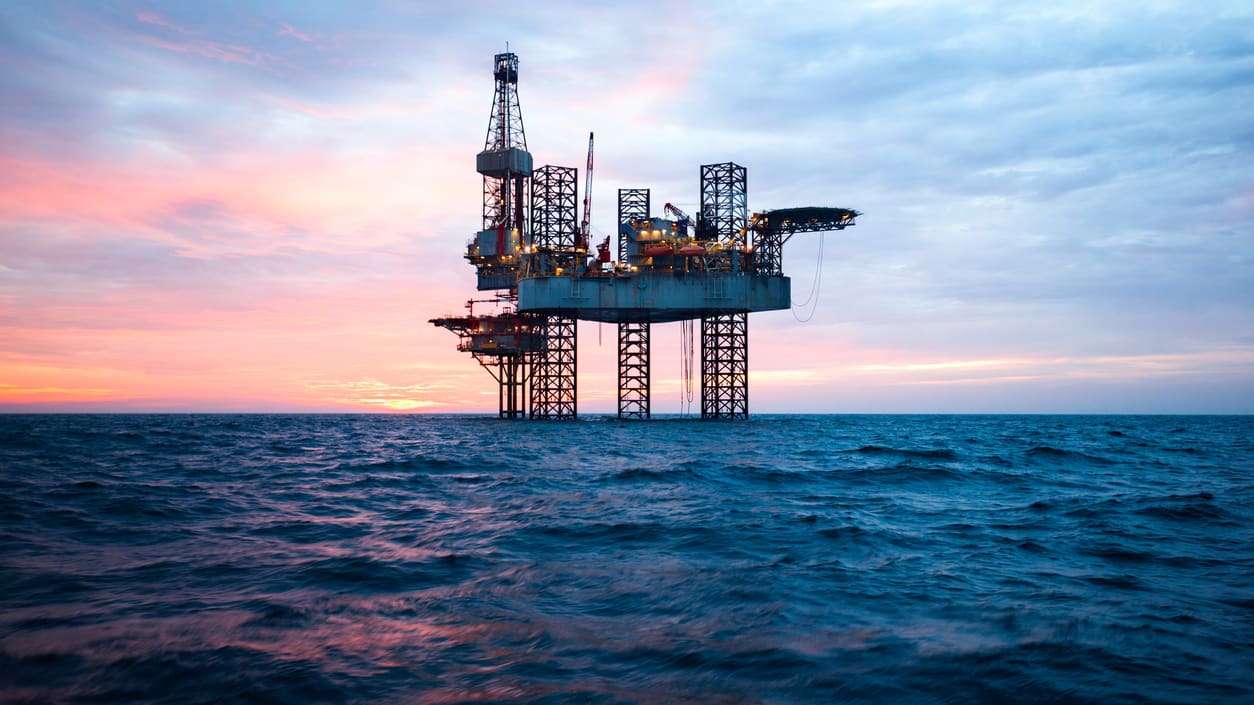 An oil rig in the ocean at sunset.