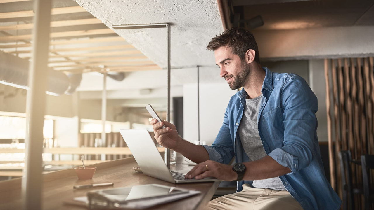 A man sitting at a table with a laptop and cell phone.