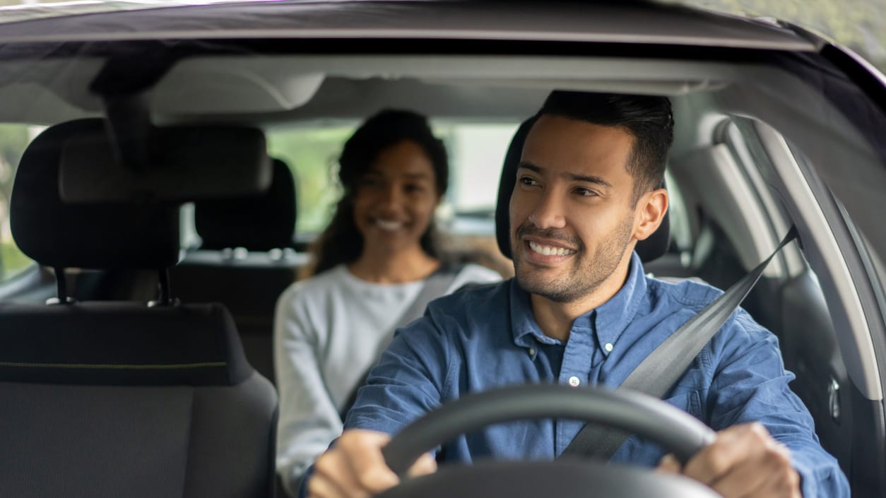 A man and woman smiling while driving a car.