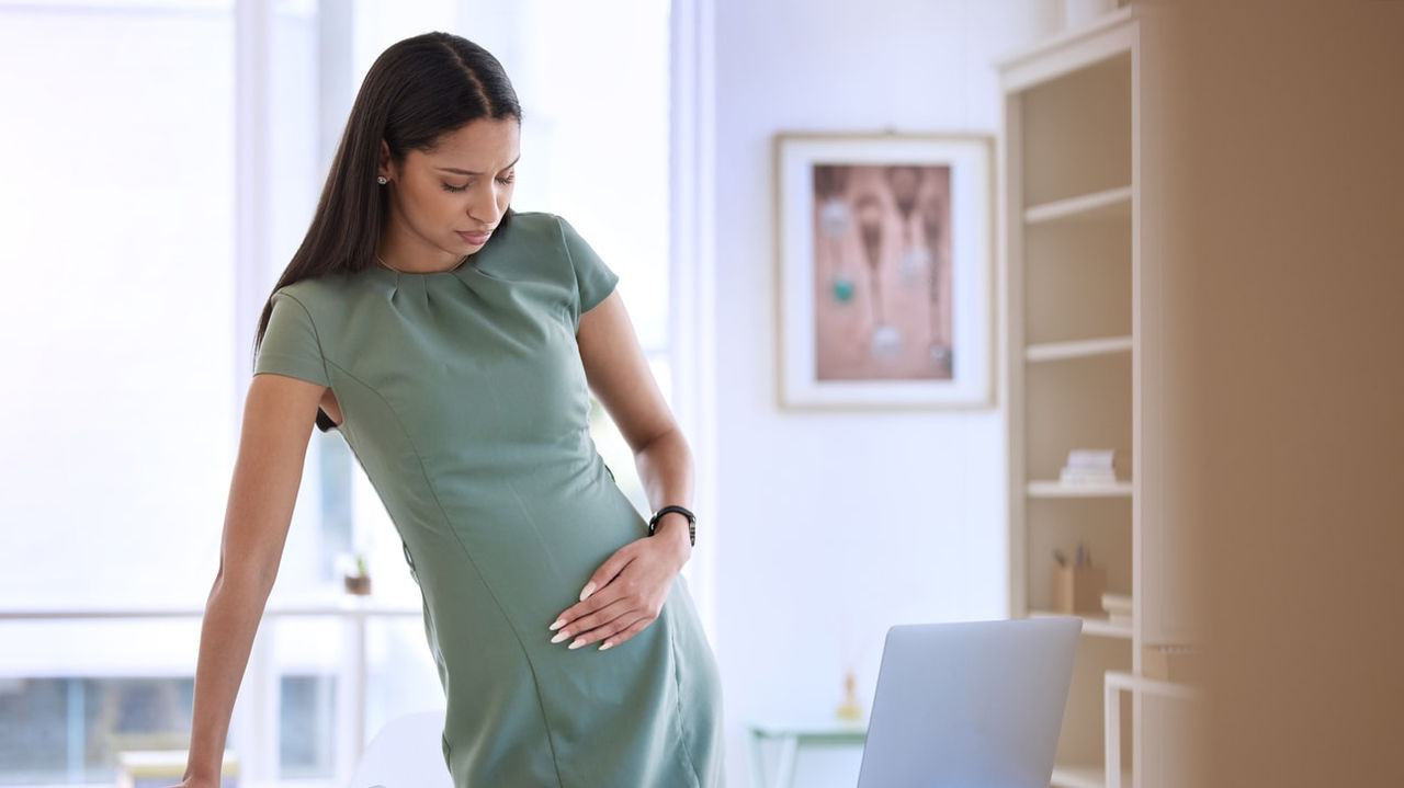 A pregnant woman sitting at a desk with a laptop.