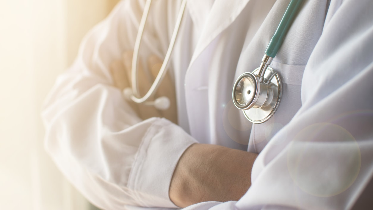 A doctor wearing a lab coat and stethoscope with arms crossed.