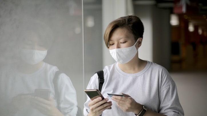 A woman wearing a face mask is using her phone.