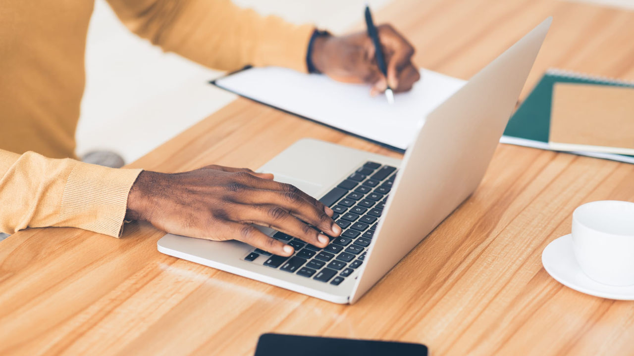 A man typing on a laptop with a cup of coffee.