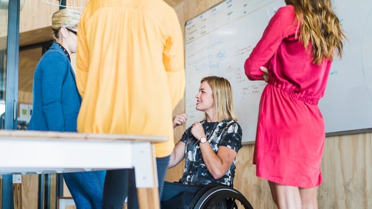 A woman in a wheelchair talking to a group of women in an office.