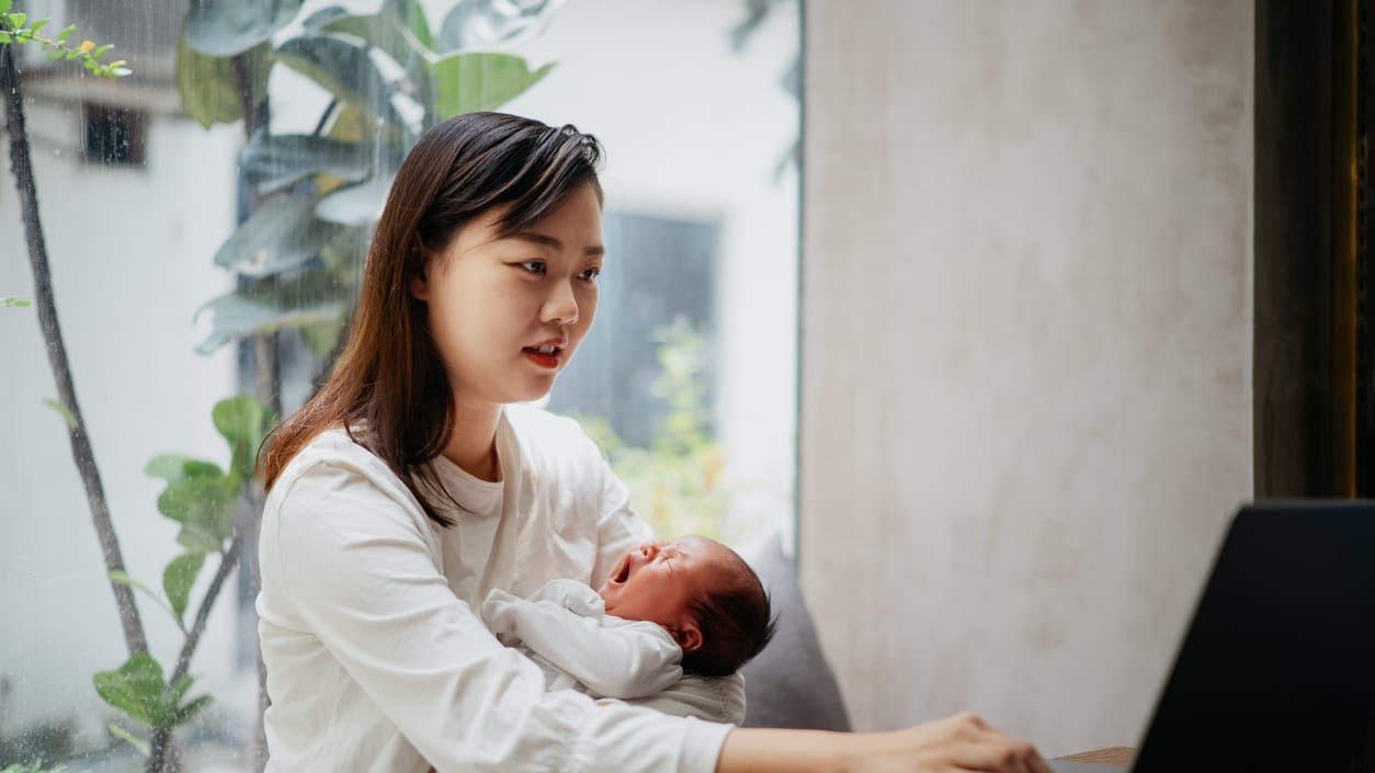 A woman holding a baby while using a laptop.