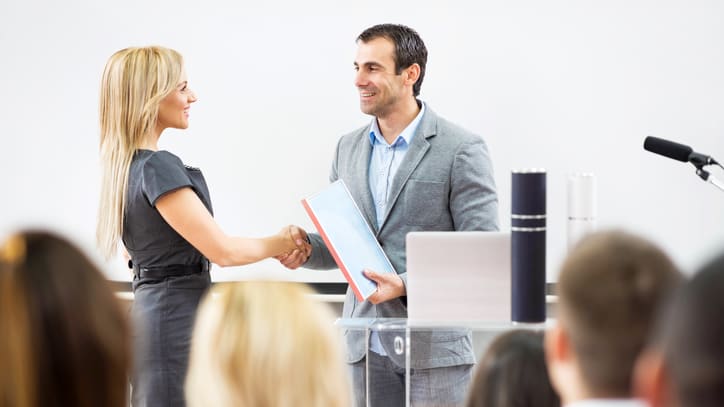 A man and woman shaking hands in front of an audience.