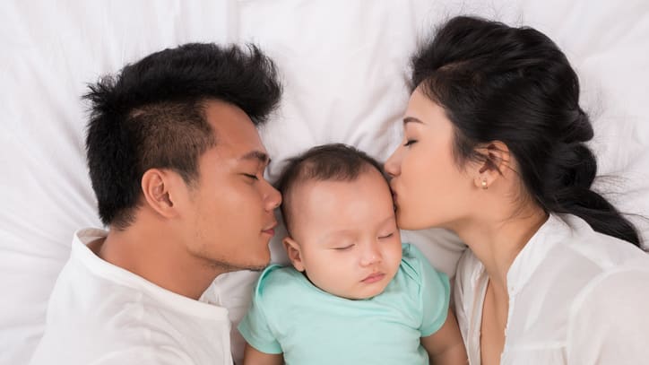 A young couple kissing their baby
