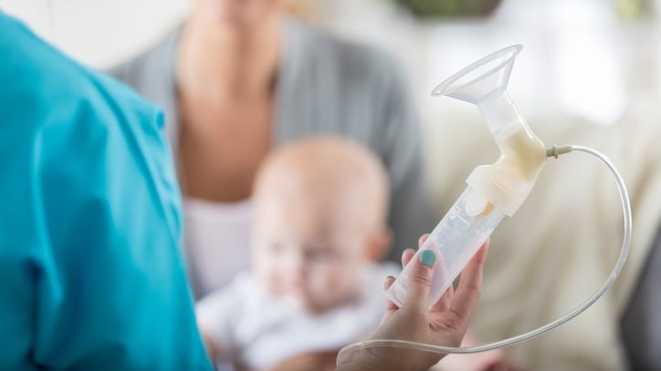 A woman is holding a baby while using a breast pump.
