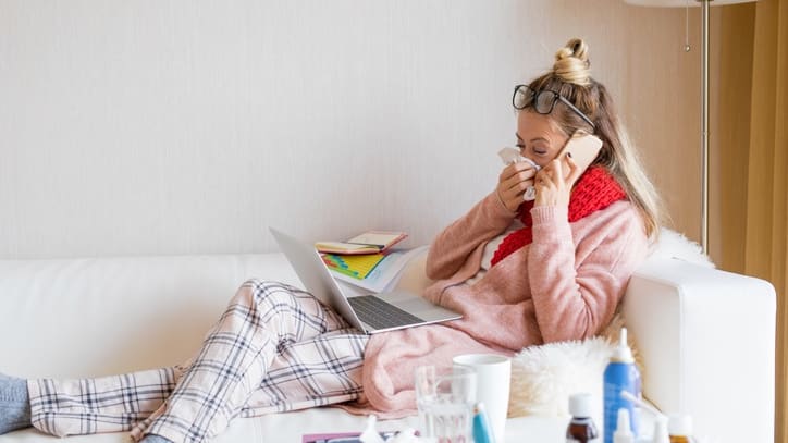 A woman in pajamas sitting on a couch with a laptop on her lap.