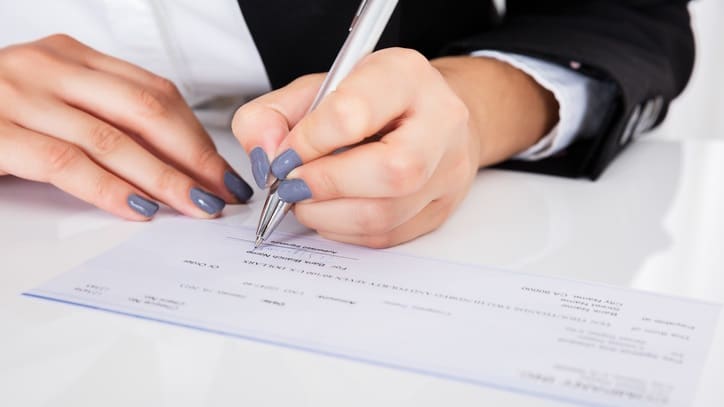 A woman signing a check at a desk.