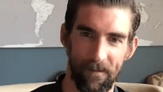 A man with a beard sitting in front of a world map.