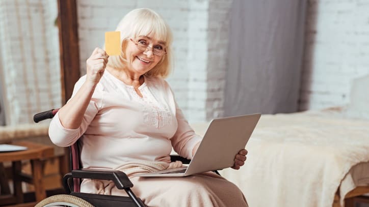 A woman in a wheelchair with a laptop and credit card.