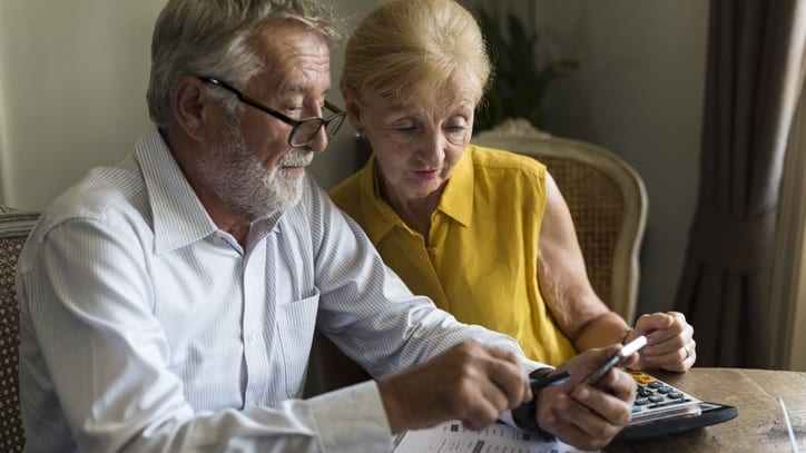 An older couple using a calculator while sitting at a table.