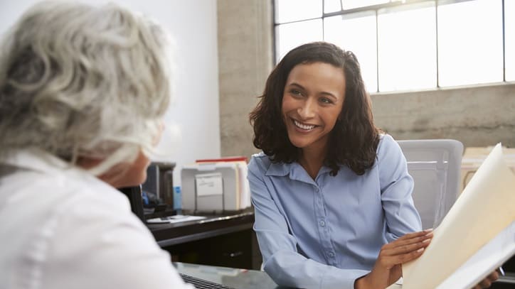 A woman sitting at a desk and talking to a woman.