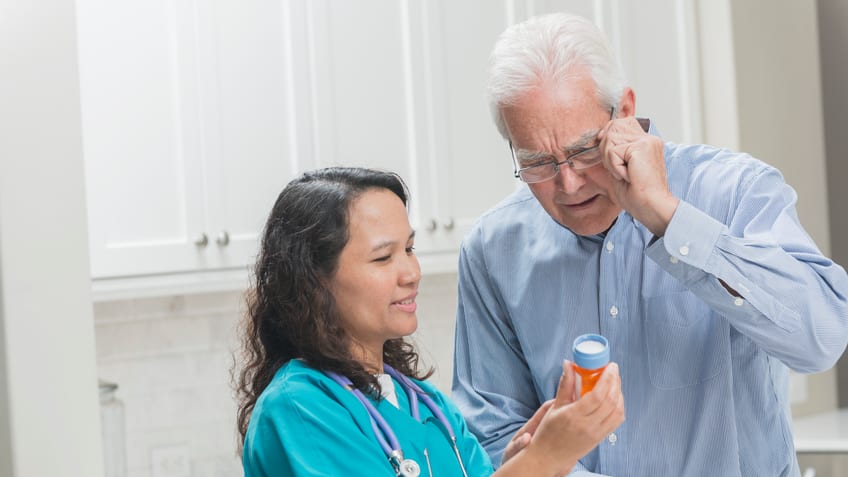 A nurse is talking to an older man in a kitchen.