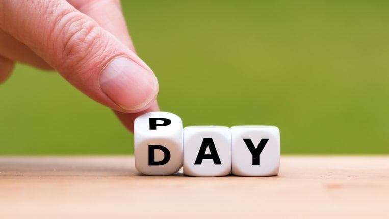 A hand is pointing to the word pay day on a wooden table.