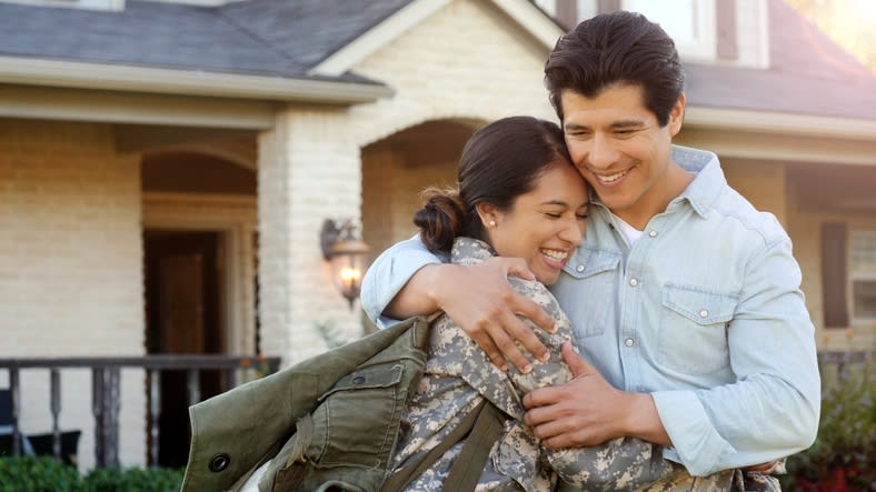 A man and woman hugging in front of a house.