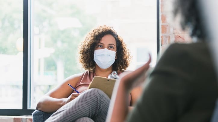 A woman wearing a surgical mask is talking to another woman.
