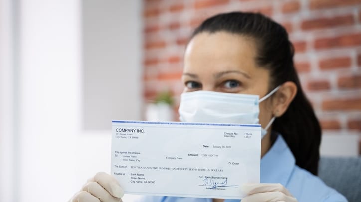 A woman in a medical mask holding up a check.